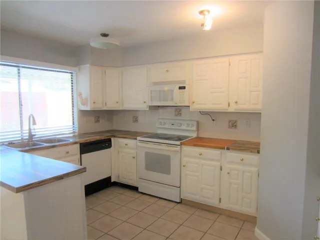 a kitchen with white cabinets appliances a sink and a window