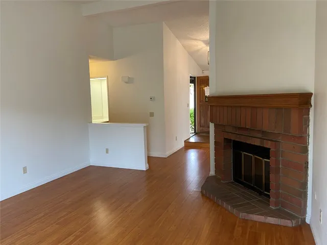 an empty room with wooden floor fireplace and windows
