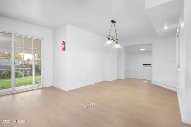 an empty room with chandelier fan and windows