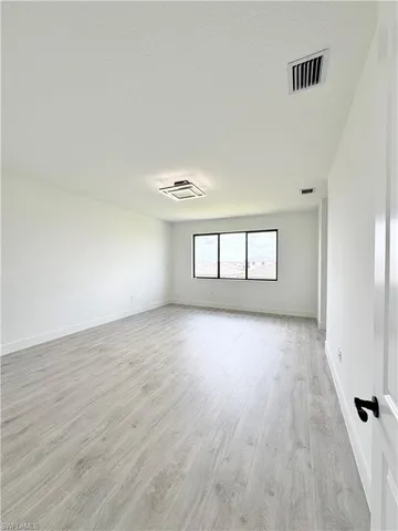 a view of an empty room with window and kitchen view