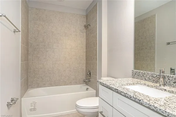 a bathroom with a granite countertop bathtub shower sink vanity and toilet