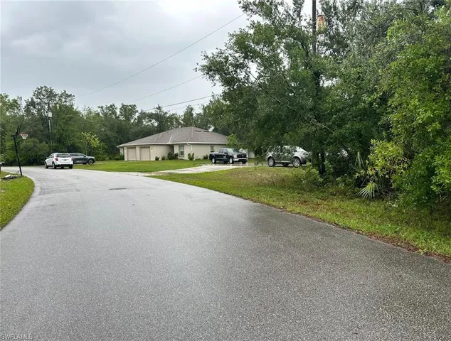 a view of a road with a yard and large trees