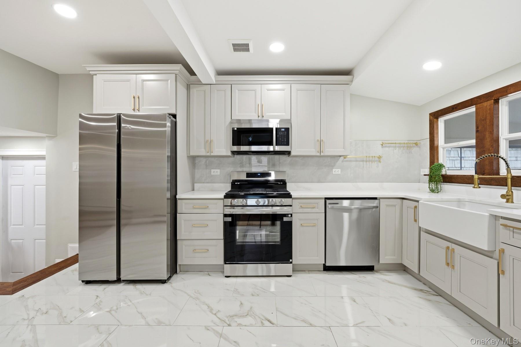 104-11 205th Street Queens, NY 11412 - Photo 14 of 50 Kitchen featuring decorative backsplash, appliances with stainless steel finishes, light marble finish flooring, recessed lighting, and white cabinetry