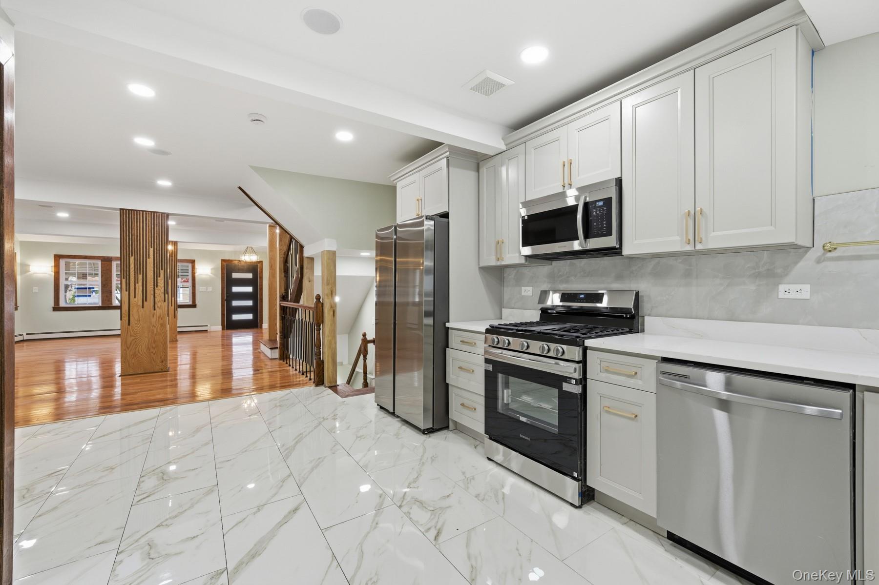 104-11 205th Street Queens, NY 11412 - Photo 17 of 50 Kitchen featuring appliances with stainless steel finishes, light marble finish floors, tasteful backsplash, white cabinets, and recessed lighting