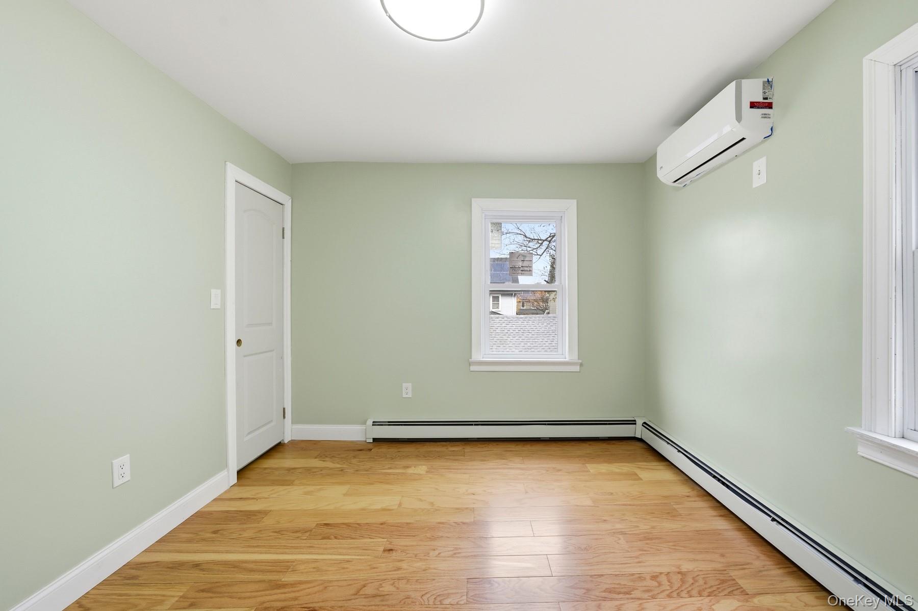 104-11 205th Street Queens, NY 11412 - Photo 25 of 50 Unfurnished room featuring a baseboard radiator, light wood-type flooring, and a wall mounted AC