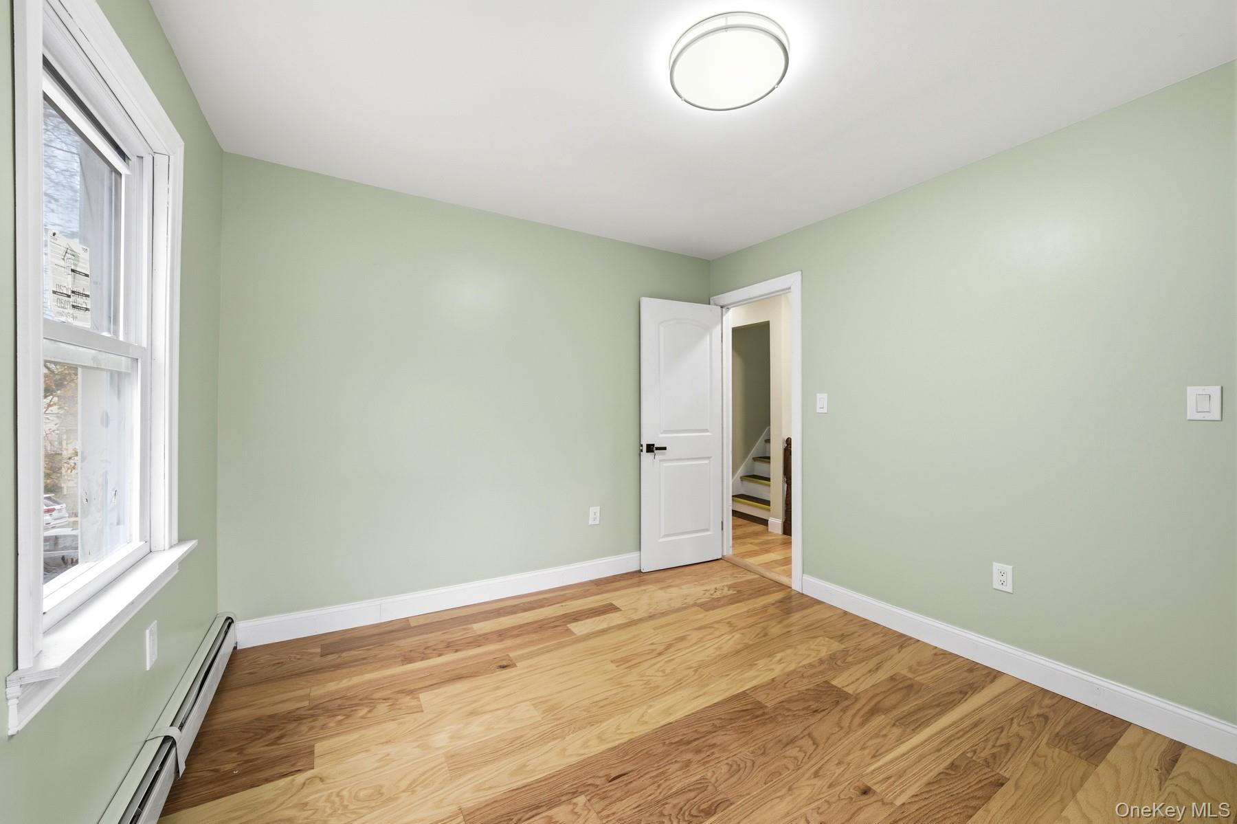 104-11 205th Street Queens, NY 11412 - Photo 26 of 50 Spare room featuring baseboard heating, wood finished floors, and stairs