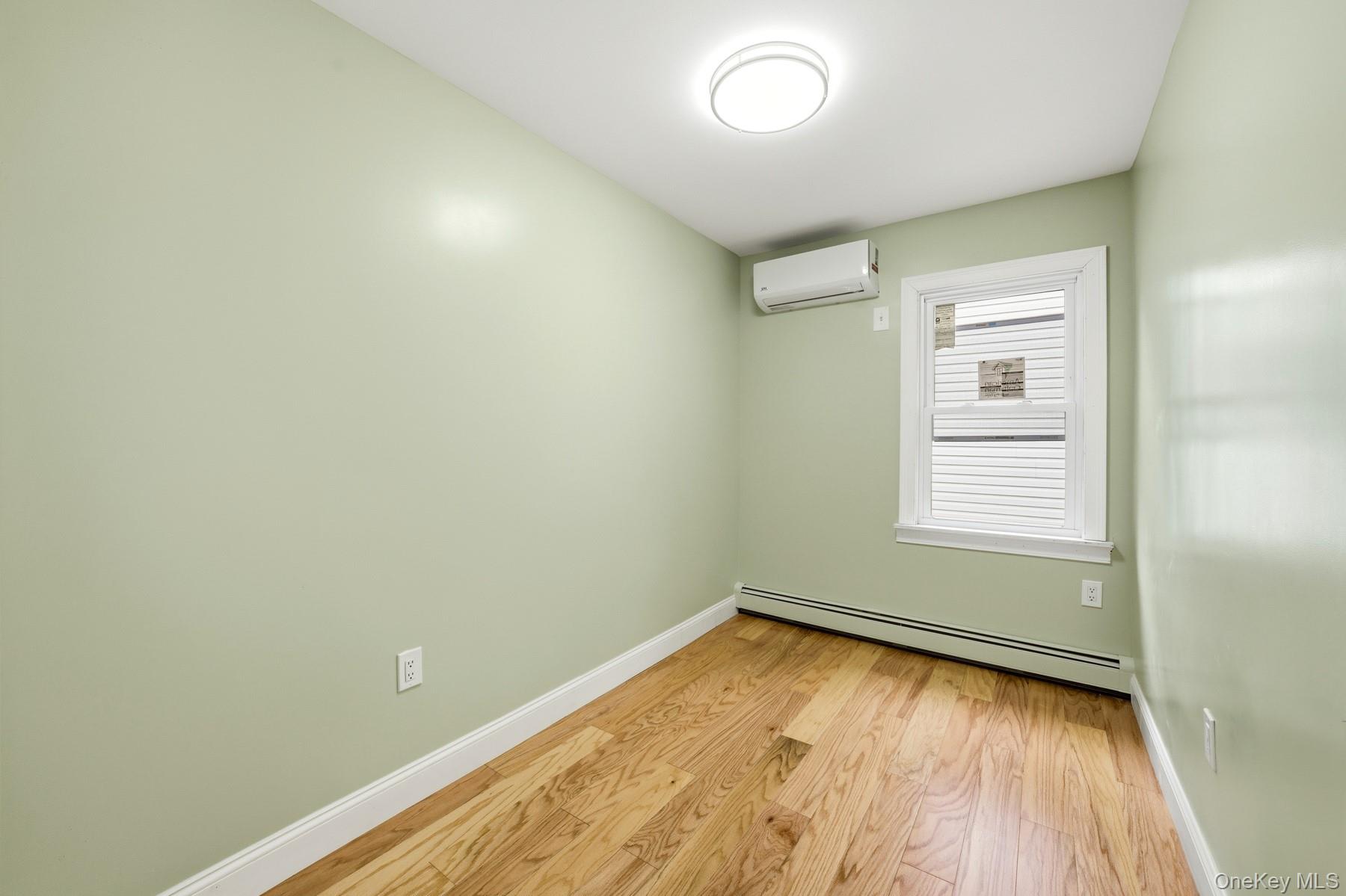 104-11 205th Street Queens, NY 11412 - Photo 27 of 50 Spare room featuring light wood finished floors, a baseboard heating unit, and a wall mounted air conditioner