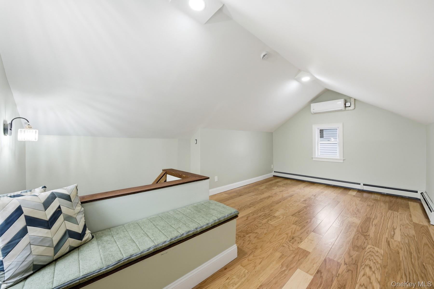 104-11 205th Street Queens, NY 11412 - Photo 34 of 50 Additional living space featuring light wood-style floors, vaulted ceiling, a baseboard heating unit, and an AC wall unit