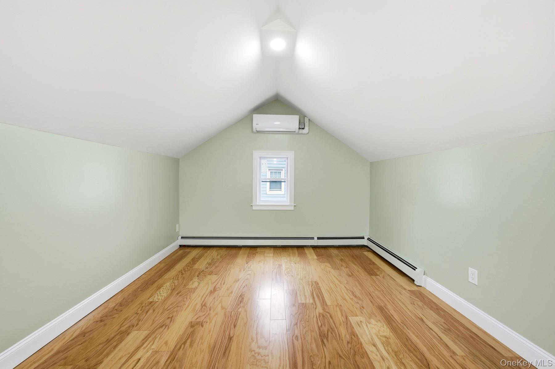 104-11 205th Street Queens, NY 11412 - Photo 35 of 50 Bonus room featuring light wood-type flooring, vaulted ceiling, baseboard heating, and a wall mounted air conditioner