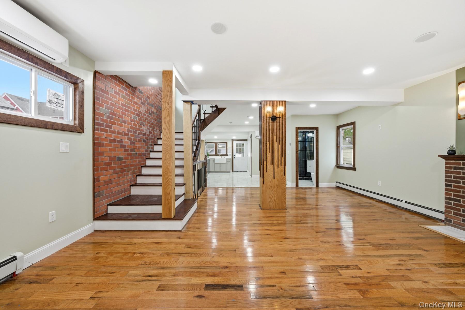 104-11 205th Street Queens, NY 11412 - Photo 6 of 50 Unfurnished living room featuring light wood-style flooring, a baseboard radiator, stairs, an AC wall unit, and brick wall