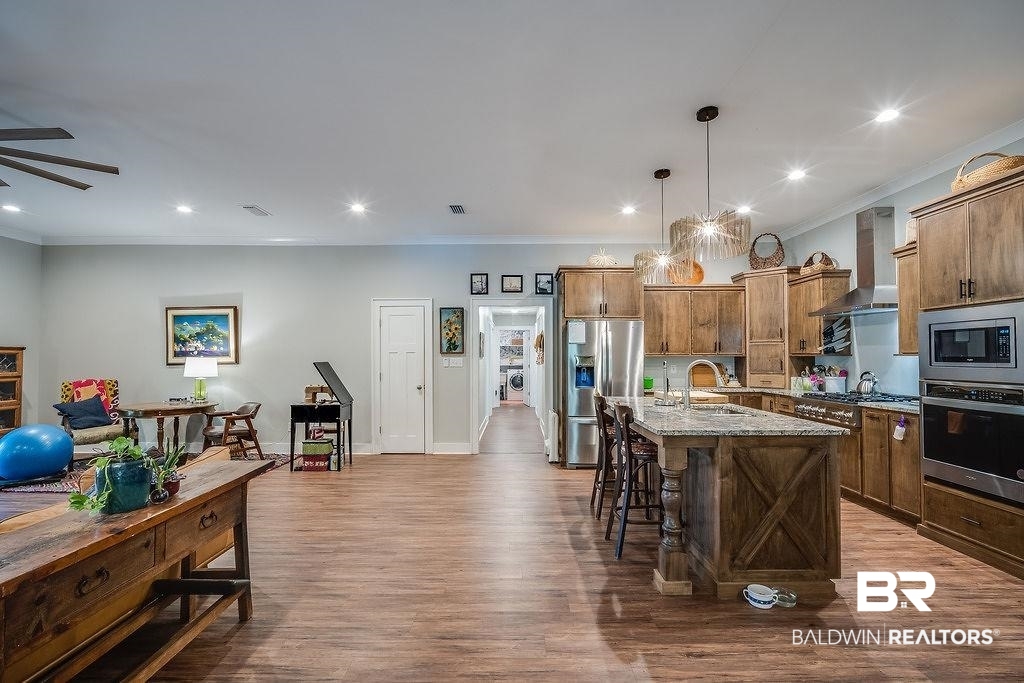 7420 Pake Road Saraland, AL 36571 - Photo 11 of 35 Kitchen with a kitchen breakfast bar, dark wood-style flooring, a sink, appliances with stainless steel finishes, and wall chimney exhaust hood