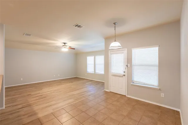 an empty room with wooden floor chandelier fan and windows