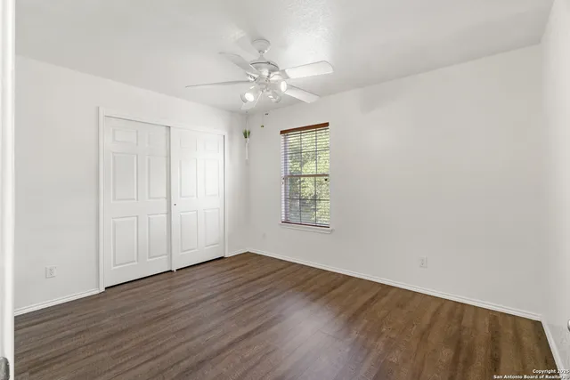 an empty room with wooden floor chandelier fan and windows