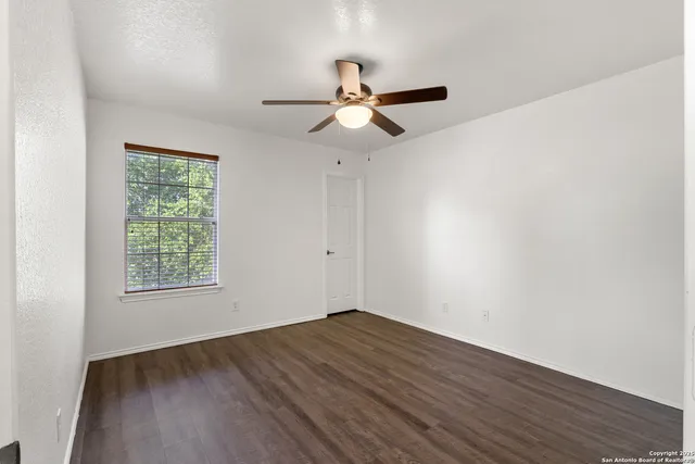 a view of empty room with wooden floor and fan