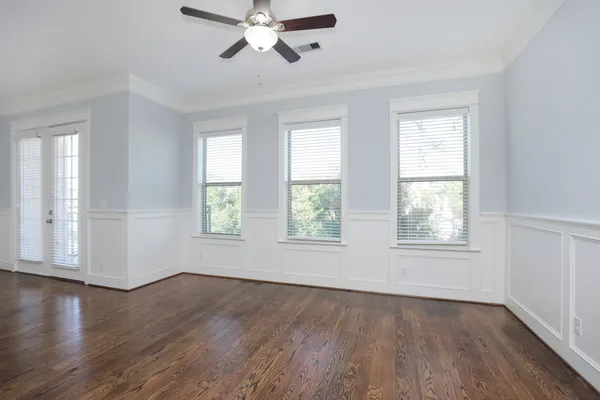 an empty room with wooden floor ceiling fan and windows