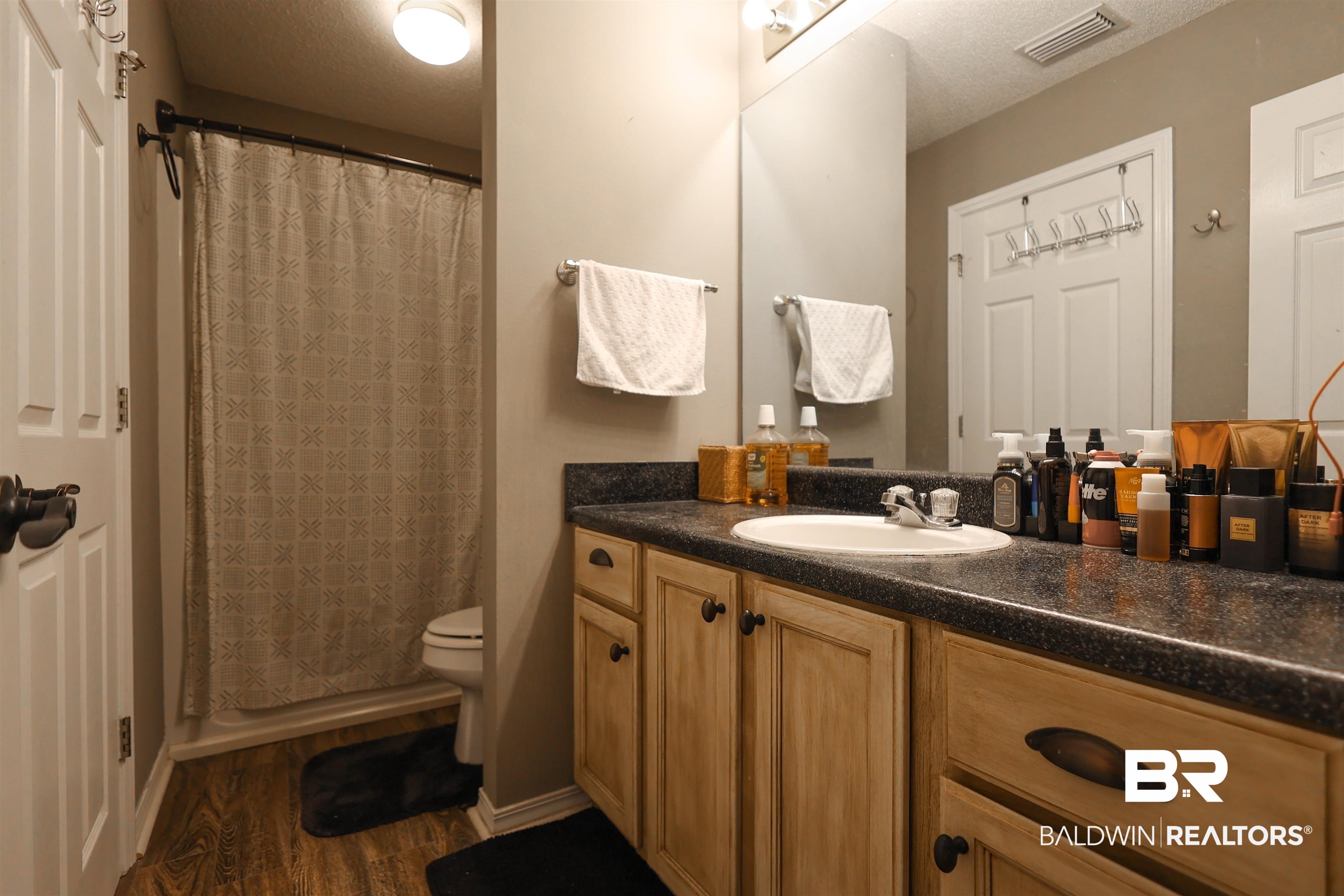 7790 Audubon Drive Foley, AL 36535 - Photo 19 of 39 Bathroom featuring a wood-finish flooring, a vanity with light wood cabinetry, a dark speckled countertop, and a built-in sink