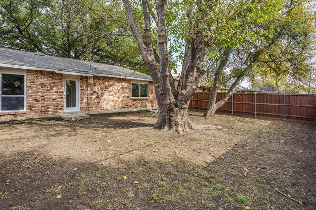 a backyard of a house with large trees and wooden fence