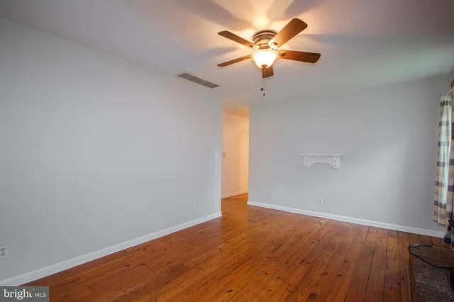 an empty room with wooden floor and a ceiling fan