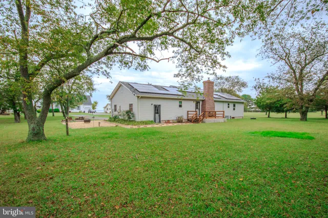 a view of a white house in front of a big yard with large trees