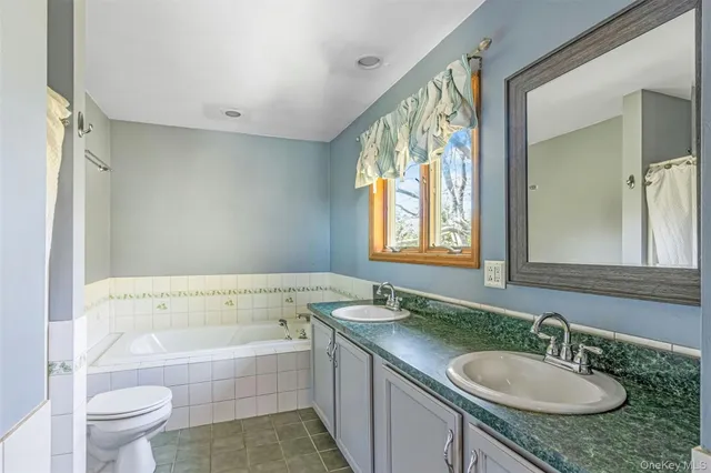 a bathroom with a granite countertop sink mirror vanity bathtub and a toilet