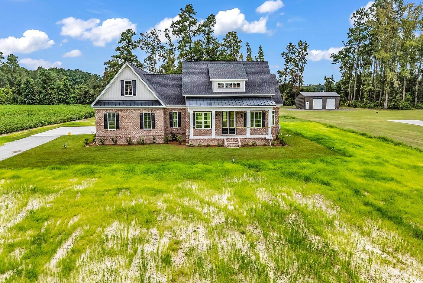 View of front of home featuring covered porch, a front lawn, a garage, an outbuilding, and brick​​‌​​​​‌​​‌‌​‌‌​​‌​​​​‌​​​‌‌​‌‌‌ siding