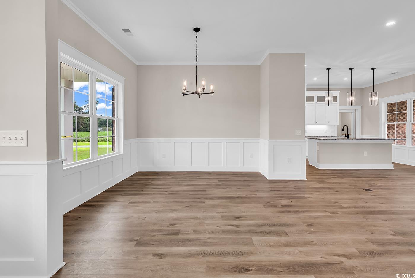 713 Horry Road Aynor, SC 29511 - Photo 3 of 40 Unfurnished dining area with wainscoting, crown molding, light wood finished floors, a decorative wall, and a chandelier
