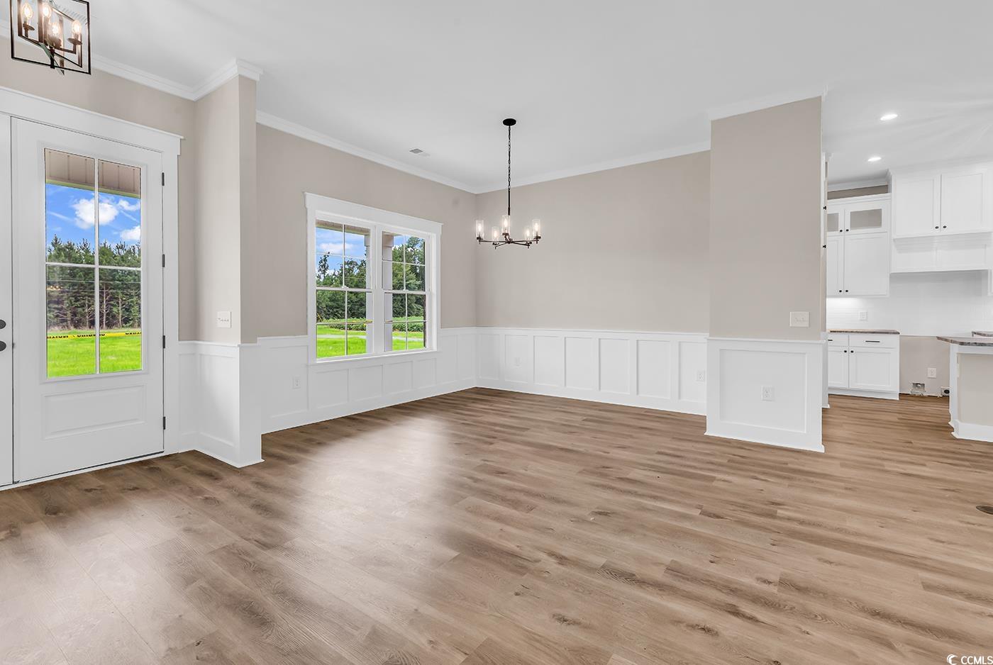 713 Horry Road Aynor, SC 29511 - Photo 4 of 40 Unfurnished dining area featuring a chandelier, light wood finished floors, a wainscoted wall, ornamental molding, and a decorative wall