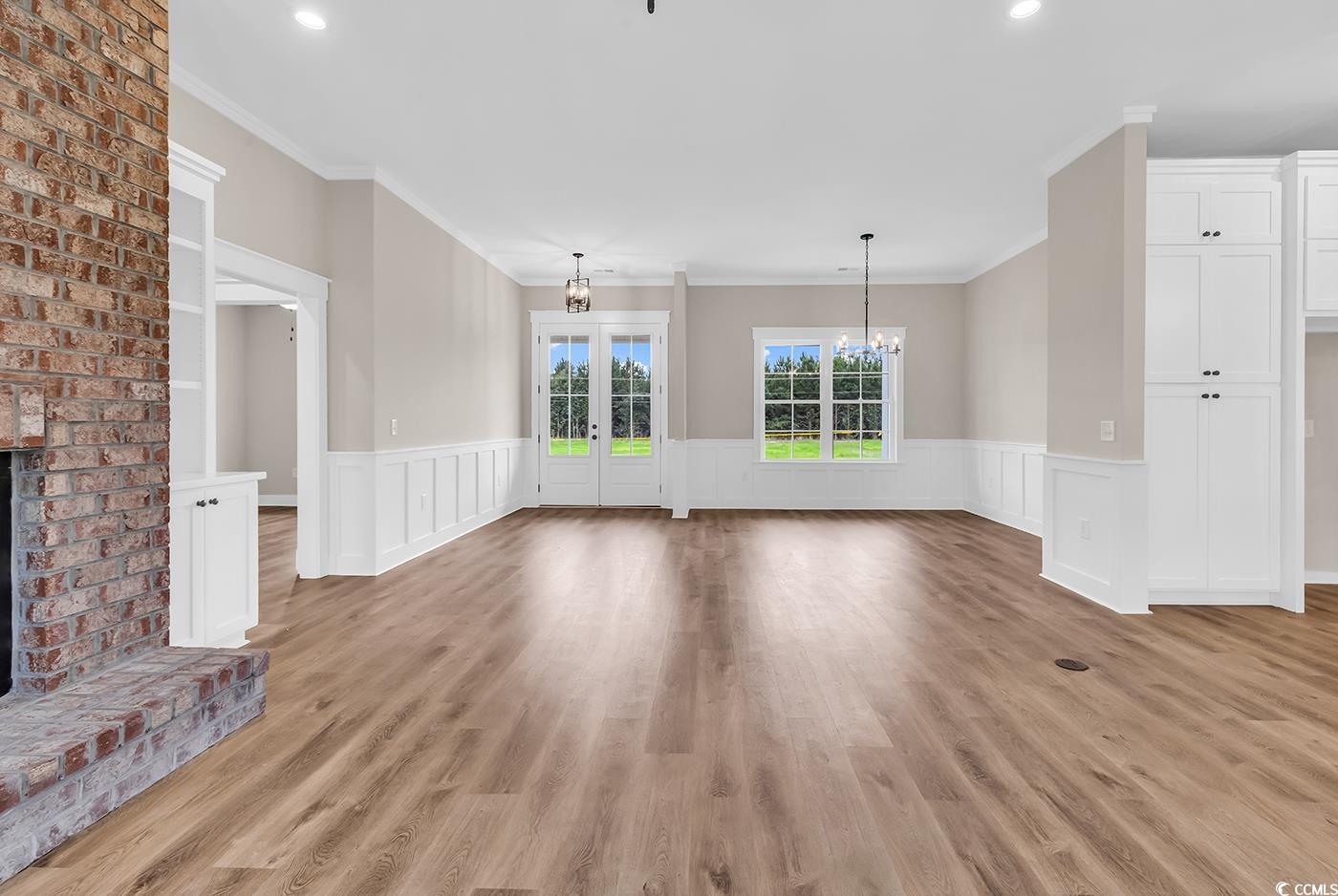 713 Horry Road Aynor, SC 29511 - Photo 9 of 40 Unfurnished living room featuring a brick fireplace, crown molding, a chandelier, light wood-style flooring, and french doors