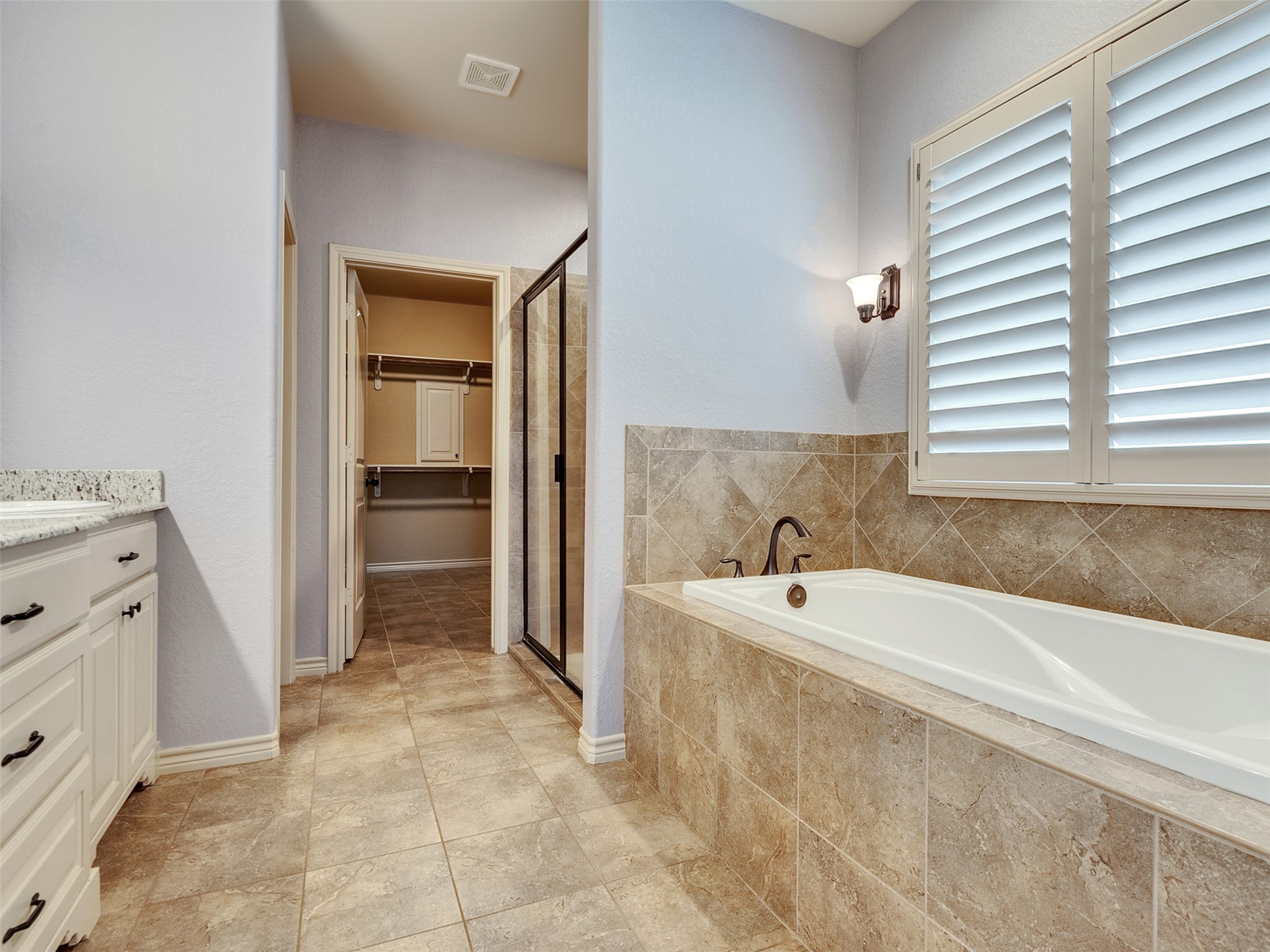 18005 Cindy Lane Conroe, TX 77302 - Photo 32 of 49 This spacious bathroom features a luxurious soaking tub with elegant tile surround, a separate glass-enclosed shower, and ample natural light from the shuttered window. It leads to a walk-in closet, offering convenience and style.