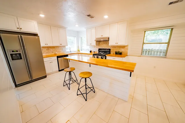 a kitchen with stainless steel appliances kitchen island granite countertop a stove a sink a refrigerator and white cabinets