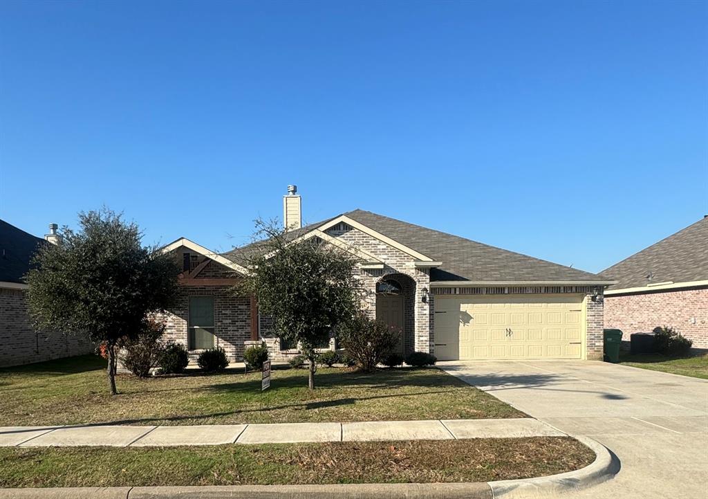 View of front of home with a front lawn, brick siding, driveway, a chimney, and an attached garage
