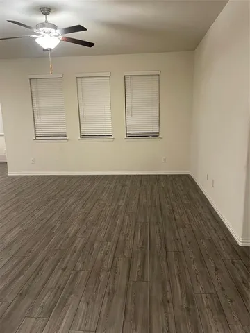 an empty room with wooden floor chandelier fan and windows