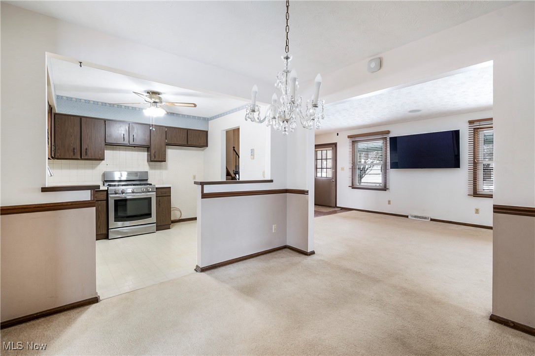 4875 New Road Youngstown, OH 44515 - Photo 20 of 25 Kitchen featuring stainless steel range with gas cooktop, pendant lighting, light carpet, ceiling fan with notable chandelier, and dark brown cabinets