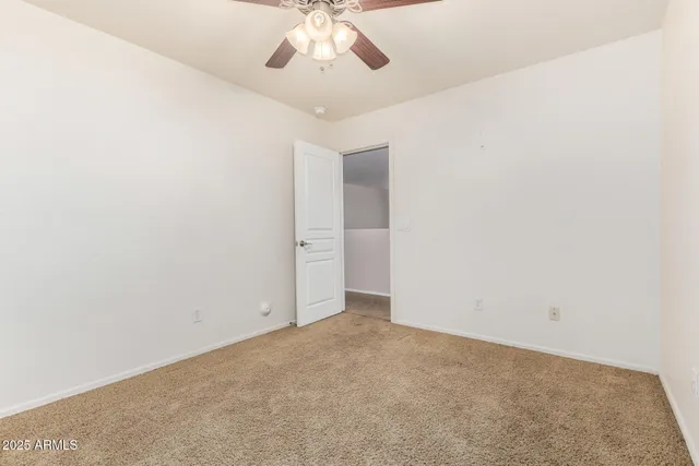 an empty room with a chandelier fan and kitchen view