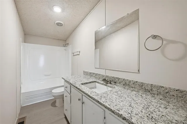 a bathroom with a granite countertop sink a toilet and shower
