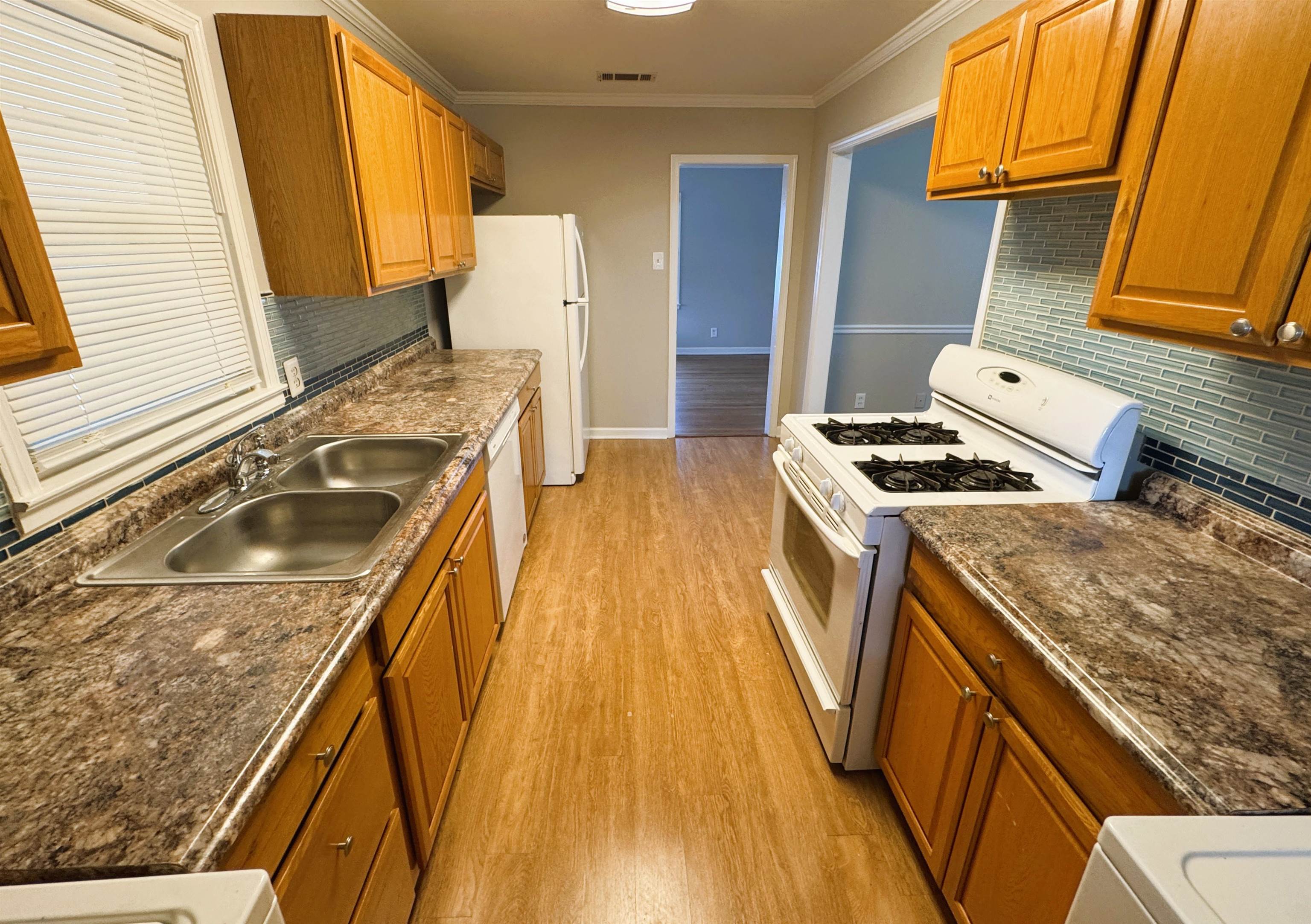 4781 Given Avenue Memphis, TN 38122 - Photo 6 of 15 Kitchen featuring white appliances, brown cabinetry, light wood-style floors, ornamental molding, and decorative backsplash