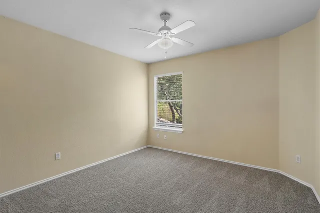 an empty room with a chandelier fan and windows