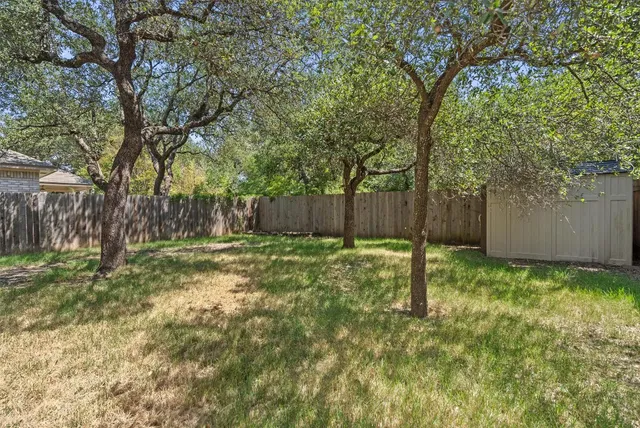 a view of a backyard with large trees and wooden fence