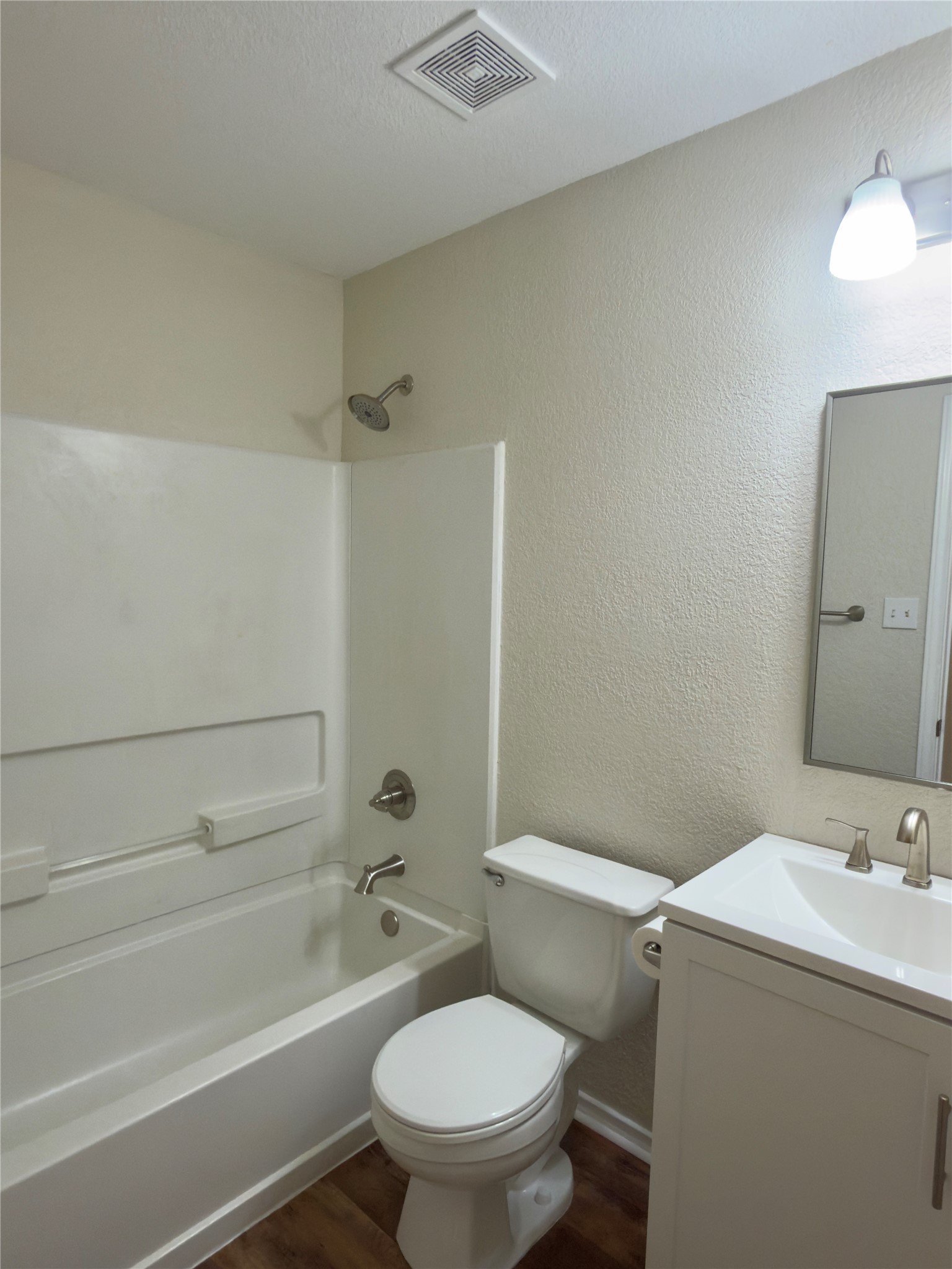 255 Myrtle Street Kyle, TX 78640 - Photo 22 of 31 Full bathroom featuring a white vanity with integrated sink, brushed nickel faucet, a toilet, a bathtub with shower, and wood-finish flooring