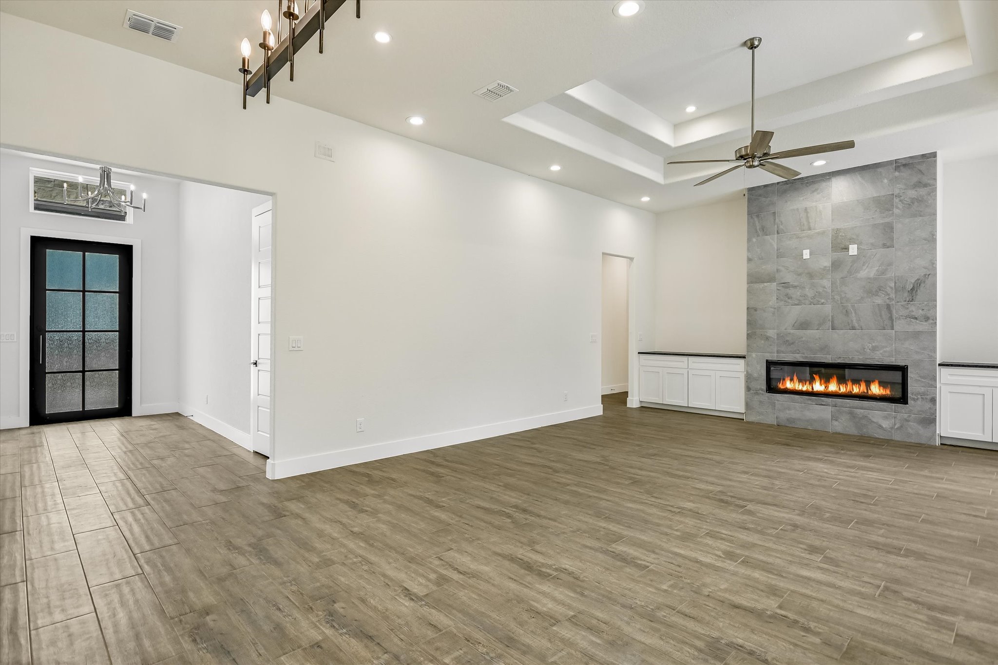 32 Peace Pipe Wimberley, TX 78676 - Photo 7 of 20 Unfurnished living room with a tiled fireplace, light wood-type flooring, hanging lights, ceiling fan, and a raised ceiling