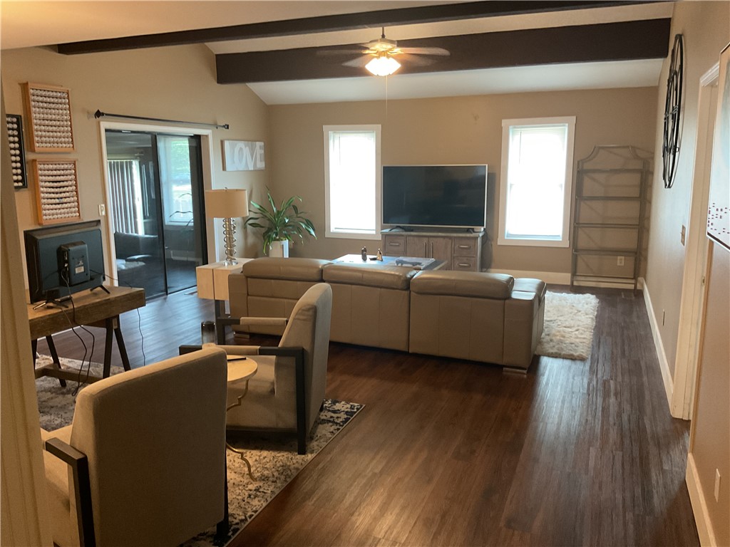 Living area featuring wood-finish flooring, vaulted ceilings with dark exposed beams, and a ceiling fan