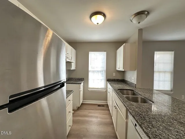 a kitchen with granite countertop a refrigerator a sink and wooden cabinets