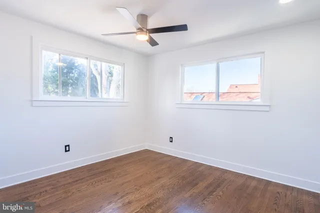 an empty room with wooden floor fan and windows