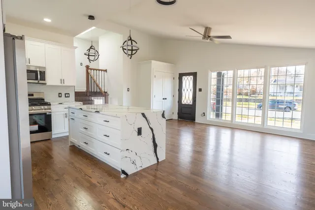 a large white kitchen with kitchen island a stove a refrigerator a oven and a large island with wooden floor