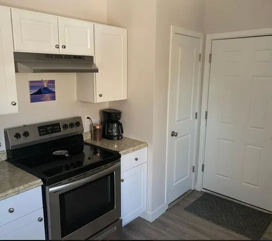 a kitchen with stainless steel appliances granite countertop white cabinets and black stove top oven with wooden floor