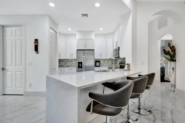 a kitchen with stainless steel appliances granite countertop a sink a stove a refrigerator and chairs