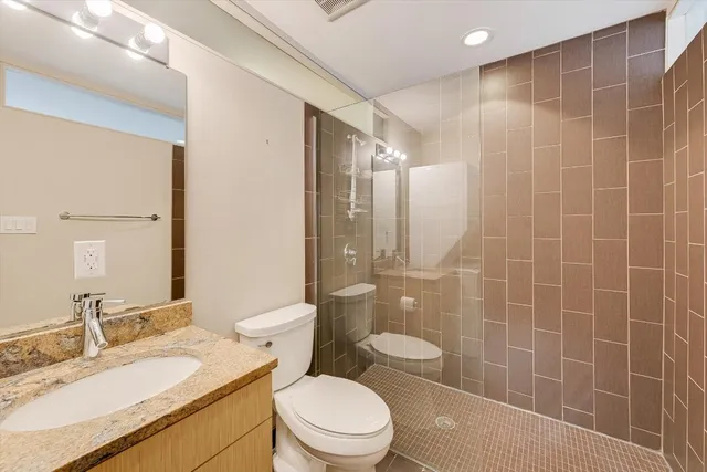 a bathroom with a granite countertop sink a toilet a mirror and shower