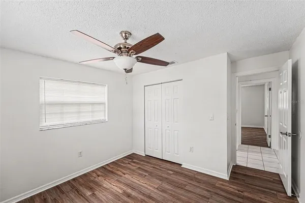a view of an empty room with wooden floor and a ceiling fan