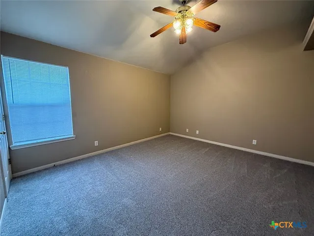 an empty room with a chandelier fan and windows