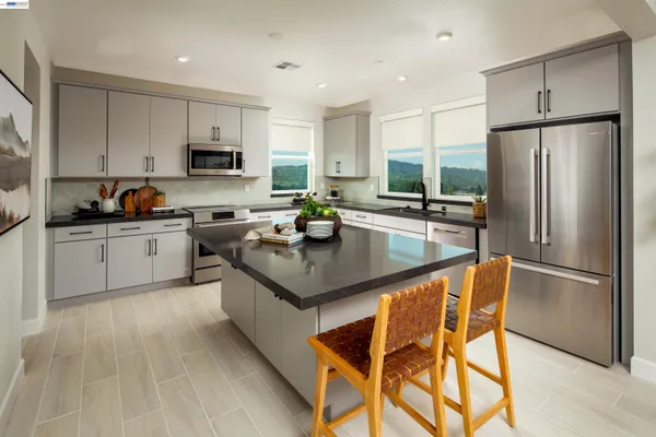 a kitchen with stainless steel appliances granite countertop a sink a stove a refrigerator cabinets and a dining table with wooden floor